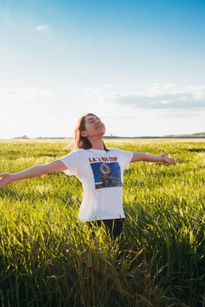 Middle-aged woman standing in a sunlit park with eyes closed, appearing calm and peaceful as she experiences emotional clarity and detoxification.